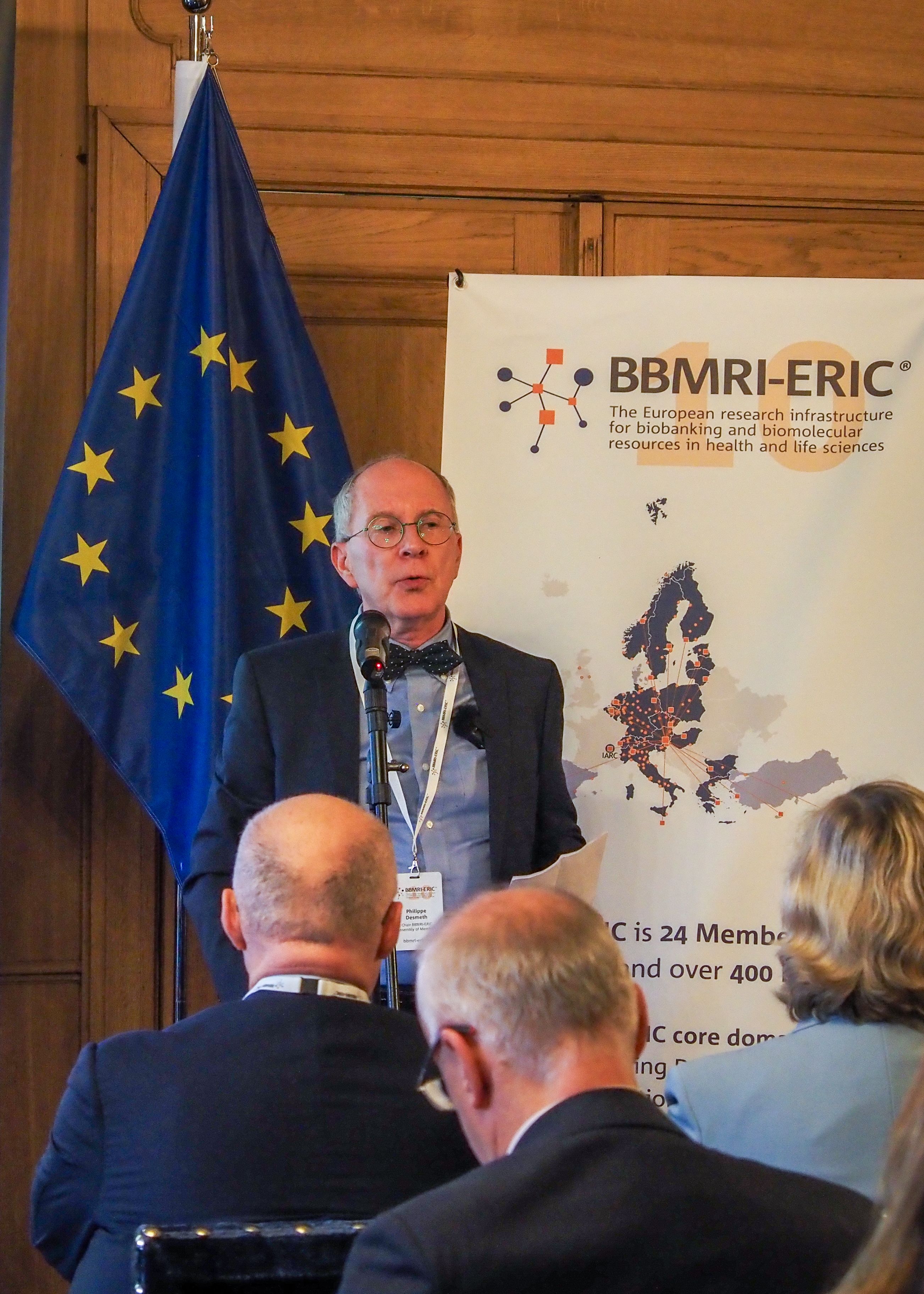 A white man wearing a suit and glasses presenting to an audience. 
