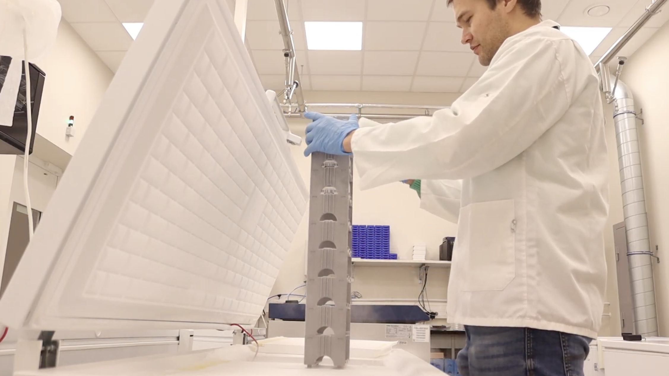 A researcher wearing a white medical gown is taking samples out of a fridge in a laboratory. 