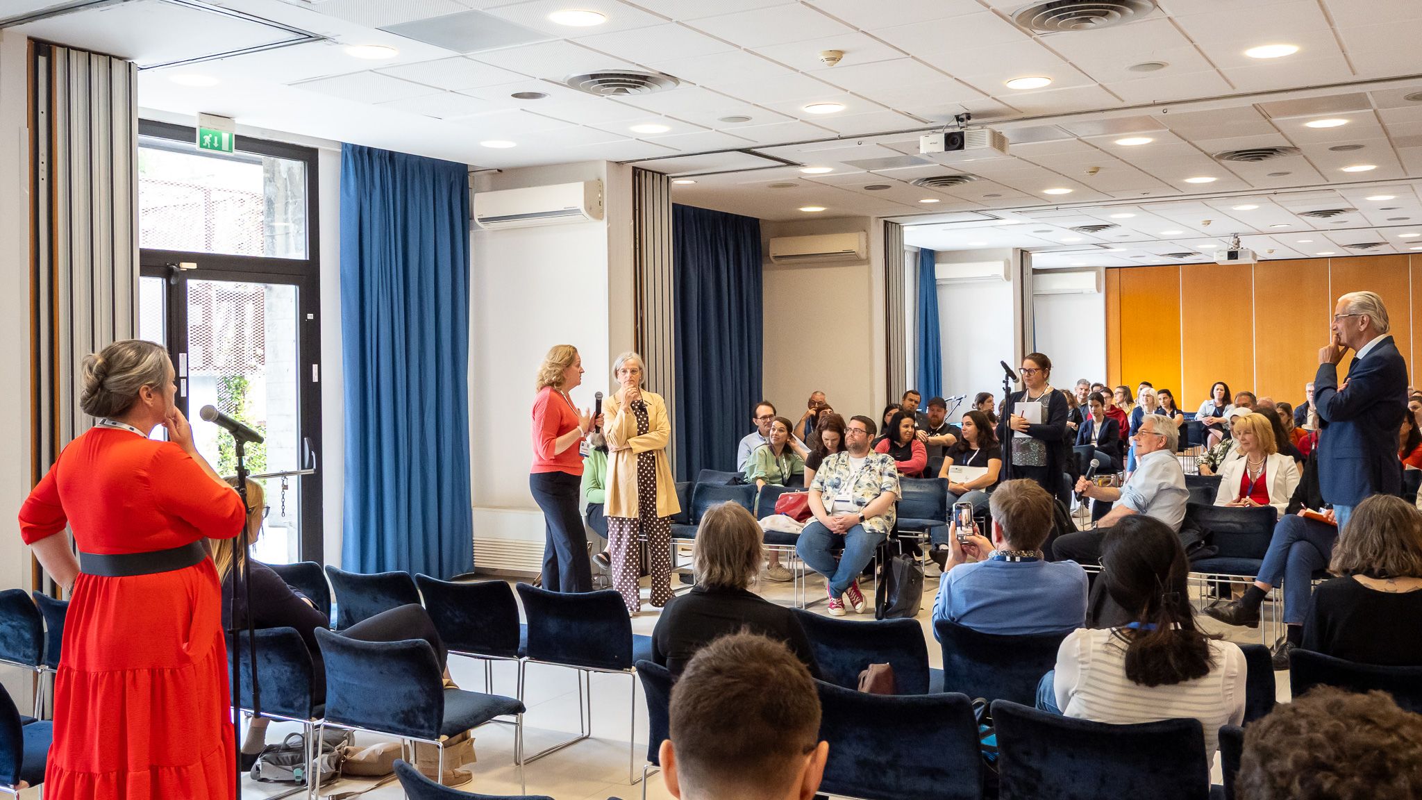 A group of people sitting and standing in a seminar room discussing.