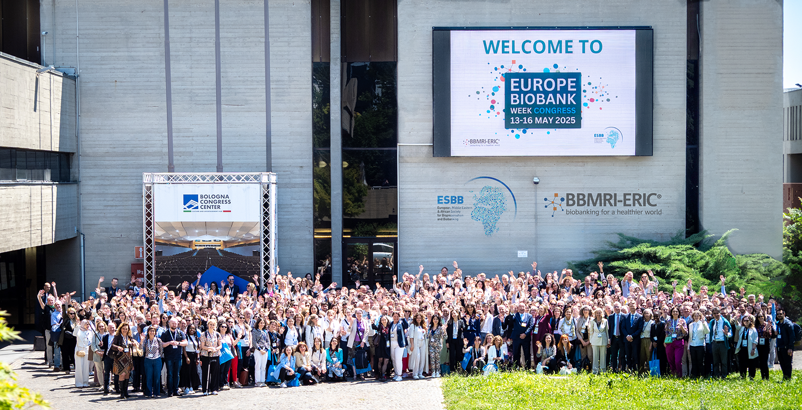 A large group of people standing in front of a conference centre waving at the camera.